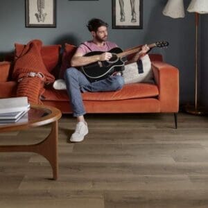 Living room with Quick-Step Brushed Oak Brown laminate flooring featuring person playing guitar on orange sofa