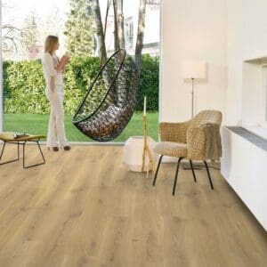 Room setting with Quick-Step Creo Tennessee Oak Natural Laminate flooring installed in a modern living space with hanging chair and garden view