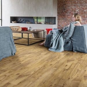 Quick-Step Alpha Blos Vintage Chestnut Natural vinyl flooring installed in a modern living room with brick wall and contemporary furniture