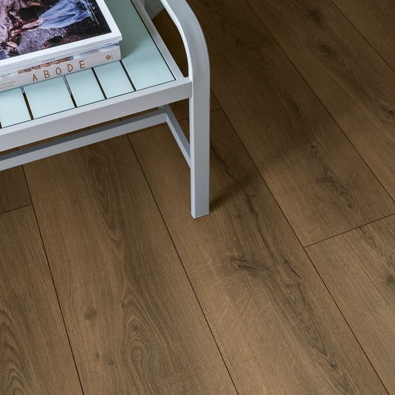 Close-up of Quick-Step Warm Brown Oak laminate flooring with water droplets demonstrating waterproof properties