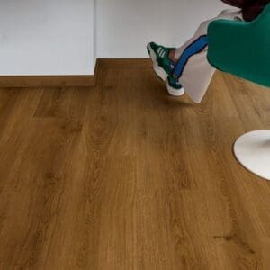 Person reading at desk with Quick-Step Botanic Caramel Oak flooring and turquoise chair