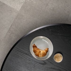 Close-up of Quick-Step Alpha Oro Concrete Rock flooring with black coffee table and croissant