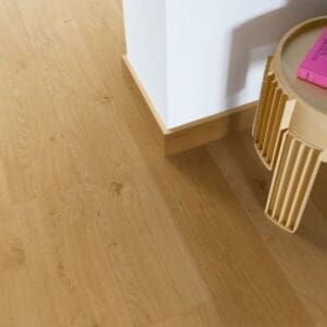 Quick-Step Alpha Blos Coast Oak Honey vinyl flooring installed in a modern living space with wooden furniture