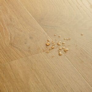 Close-up of Quick-Step Alpha Blos Coast Oak Honey vinyl flooring showing water droplets demonstrating waterproof properties