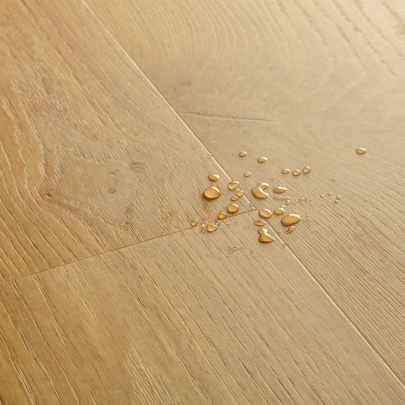 Close-up of Quick-Step Alpha Blos Coast Oak Honey vinyl flooring showing water droplets demonstrating waterproof properties