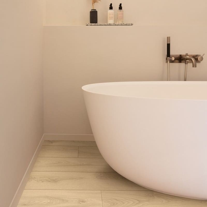 Bathroom installation of Quick-Step Desert Greige Oak laminate flooring with freestanding bathtub showing practical application