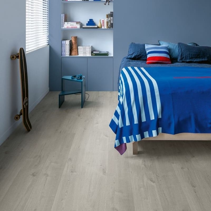 Quick-Step Alpha Bloom Cotton Oak Cold Grey flooring installed in a modern blue bedroom with built-in shelving
