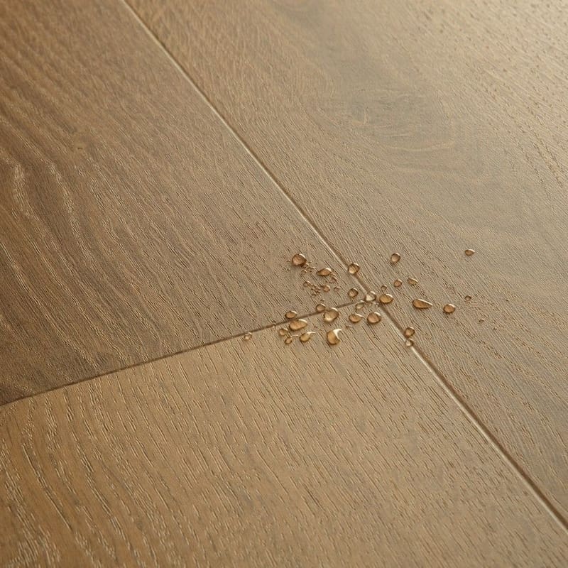 Close-up of Quick-Step Alpha Bloom Elegant Oak Fumed vinyl flooring showing water-resistant properties with water droplets on surface