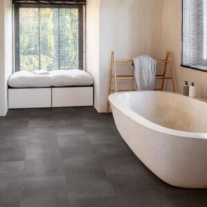Modern bathroom with Quick-Step Alpha Oro Volcanic Rock flooring installed, featuring freestanding bath and window seat