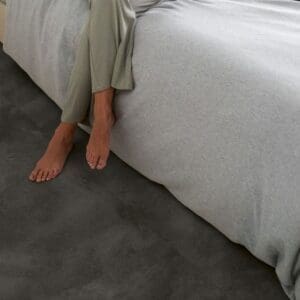 Person sitting on bed with Quick-Step Soft Graphite vinyl flooring in a modern bedroom