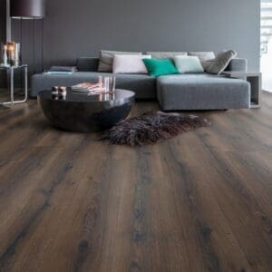 Quick-Step Majestic Desert Oak Brushed Dark Brown laminate flooring installed in a contemporary living room with grey furniture