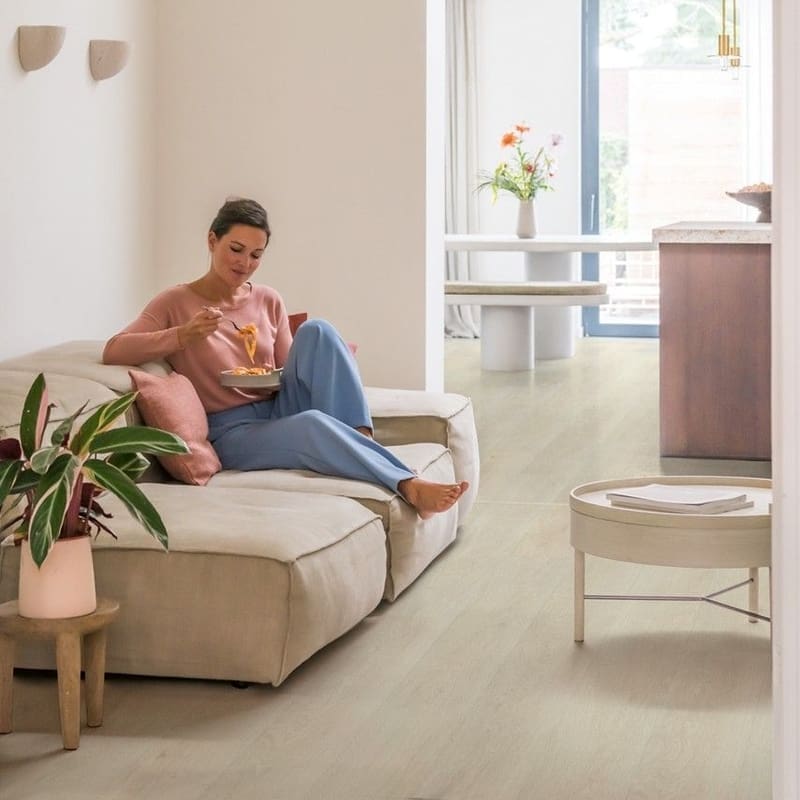 Living room with woman relaxing on sofa and light oak vinyl flooring