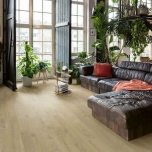 Modern living room with large windows featuring Quick-Step Soft Oak Medium laminate flooring and leather sectional sofa