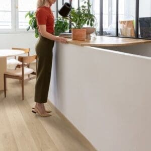 Person watering plants in kitchen with Quick-Step Alpha Blos Coast Oak Sand flooring