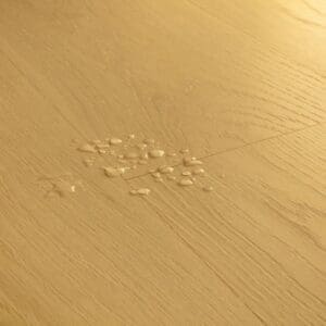 Detail view of Quick-Step Classic Biscuit Brown Oak laminate showing water droplets demonstrating waterproof feature