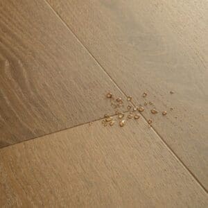 Close-up of Quick-Step Alpha Bloom Elegant Oak Fumed vinyl flooring showing water-resistant properties with water droplets on surface